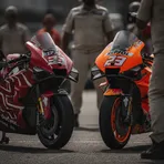Two competing MotoGP motorbikes are parked next to each other in the pit lane after a hard-fought race.
