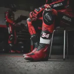 A close-up on the leg and boot of a MotoGP rider resting in the pit garage, suggesting recovery from an injury.