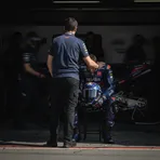 A MotoGP rider being comforted by a team member in the Aprilia pit garage.