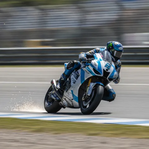A MotoGP rider in a blue and silver custom livery leans at an extreme angle through a corner, with sparks flying from their knee slider on the track.