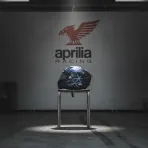 A lone racing helmet rests on a stool in an otherwise empty and quiet MotoGP pit garage, signifying a rider's absence due to injury.