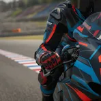 A close-up view of a MotoGP rider's hand on the handlebars, showing the intense focus required to ride at the limit.