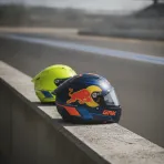 A fluorescent yellow helmet and a dark blue and orange helmet sit together on a pit wall, symbolising the rider moves between the VR46 and KTM teams.