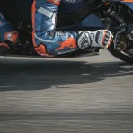 A close-up view of a MotoGP rider's arm and gloved hand, showing the extreme muscle tension required to control the bike.