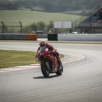 A rider on a red MotoGP bike leans at an extreme angle through a corner during a race.