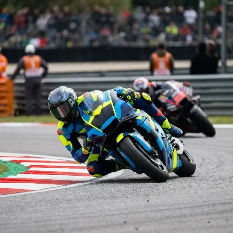 A MotoGP rider performs an aggressive out-braking manoeuvre, diving up the inside of a rival into a tight corner.