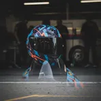 A MotoGP rider sits on his motorcycle in the pit garage, his helmet reflecting the lights, conveying intense focus before a race.