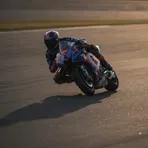 Marco Bezzecchi celebrates a victory on the MotoGP podium, holding a trophy aloft amidst falling confetti.