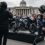 A modern MotoGP motorcycle on display in a famous London square, surrounded by members of the public.