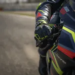 A close-up photograph of a MotoGP rider's gloved hand under strain as it grips the handlebar of their racing motorcycle.