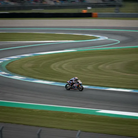 An aerial view of a race track corner with a graphic overlay illustrating the optimal racing line from the outside edge to the inside apex.