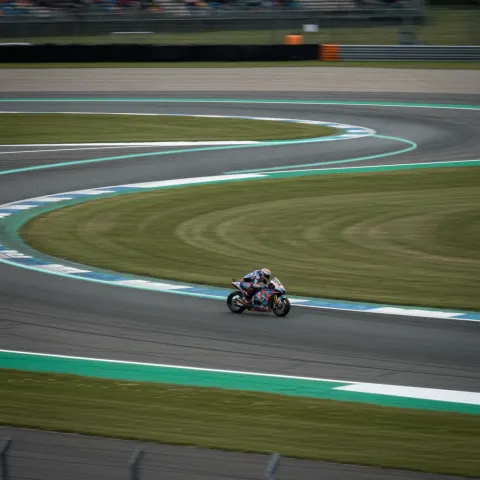 An aerial view of a race track corner with a graphic overlay illustrating the optimal racing line from the outside edge to the inside apex.