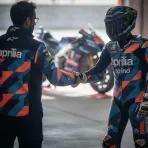 A rider and a team manager shaking hands in a MotoGP pit garage to signify a new contract agreement.