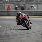 A MotoGP rider leans hard into a corner, with the rear of the bike sliding out in a controlled and dramatic fashion.