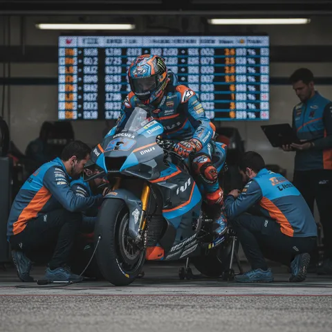 A MotoGP rider sits on his bike in the pit garage, surrounded by his team during a tense qualifying session.