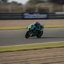 A MotoGP rider leans their bike at a sharp angle while navigating a fast, flowing corner at the Silverstone circuit.